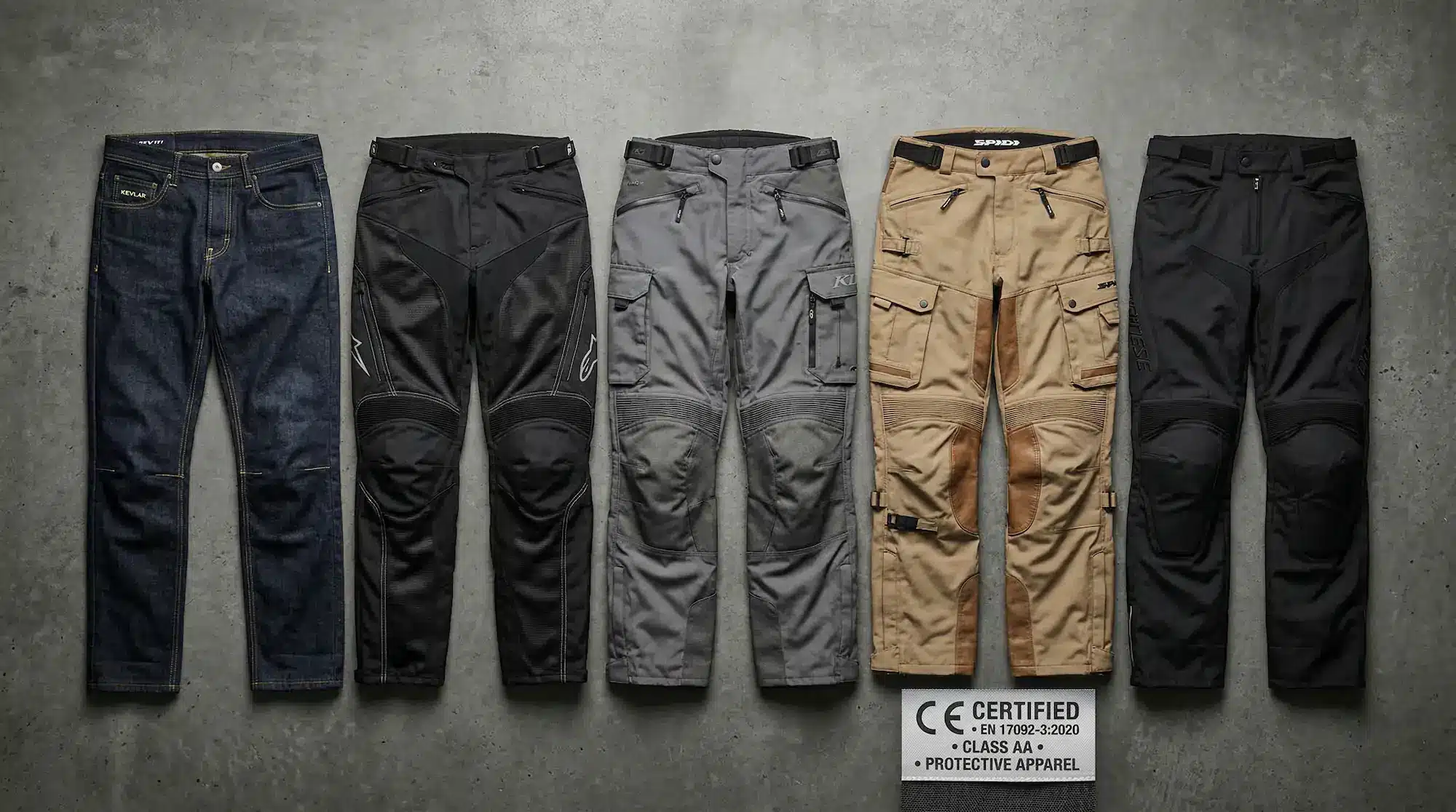 Five types of men's motorcycle riding pants laid out side by side from casual Kevlar jeans to ADV touring pants with CE certification tag visible