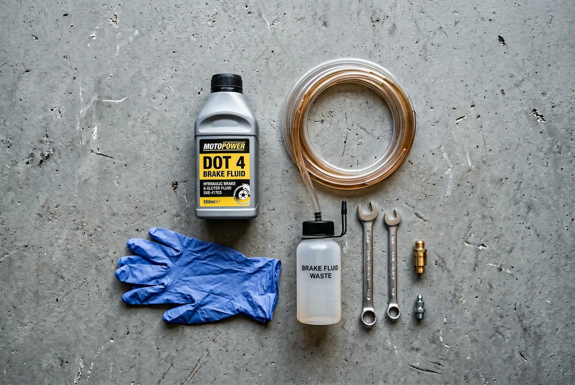 Motorcycle brake bleeding tools laid out on a workbench including DOT 4 fluid, bleed hose, and wrenches