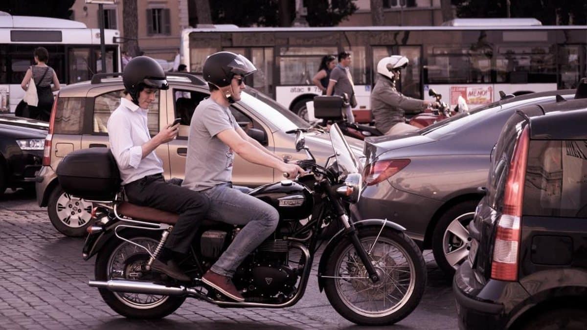 Riders on a motorcycle passing between cars in slow traffic